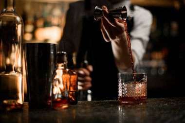 Kadın eli, barın tezgahına kokteyl hazırlamak için jigger 'dan bardağa alkollü bir içecek doldurur.