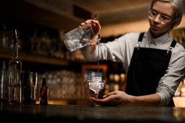 Bardaklı barmen bardaktaki son temiz içkiyi karıştırıcı bardaktan büyük bir buz kalıbına doldurur.