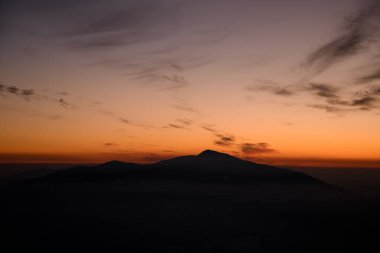 Karanlık dağ silueti parlak turuncu günbatımı gökyüzüne karşı ağırlıksız bulutlarla. Güzel doğanın kaliteli görüntüsü.