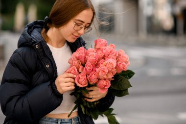 Bir sonbahar günü, bir portre fotoğrafında sokakta duran şefkat dolu kızın ellerinde pembe çiçekler.