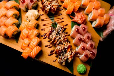 Suşi sanatını bir dizi ton balığı, susam ve teriyaki dürümleri eşliğinde doğal, yeşil yapraklara yerleştirilmiş ve yanında bir tutam wasabi....