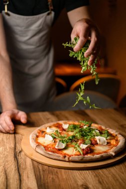 Şeflerin aşçılık sanatına tanık olun. Pizzanın üzerine ustalıkla taze roka serpiştiriyorlar. Görsel çekiciliğini ve tadını arttırıyorlar..