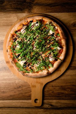 Taze ve lezzetli bir pizzanın yakın görüntüsünün tadını çıkarın, ahşap bir tahtanın üzerine roka eklenerek yükseltilmiş..