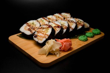 Kahverengi sos, wasabi, zencefil turşusu ve beyaz pirinçle Norveç suşisine sarılmış. Siyah arkaplandaki tahta tahta.