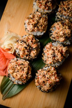 Koyu dokulu ahşap bir tahta üzerinde suşi. Somon, zencefil turşusu, havyar ve yeşil yapraklı sıcak baharat.