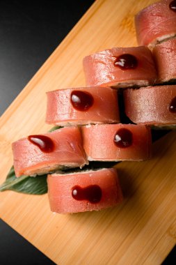 Büyük yeşil bir yaprağın üzerinde somon balığına sarılmış soya sosu. Siyah arka planda suşi.