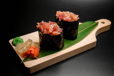 İki rulo Norveç 'e sarılmış kırmızı deniz balığıyla ahşap bir tahtada sıcak wasabi ve yeşil yapraklı zencefil turşusu.