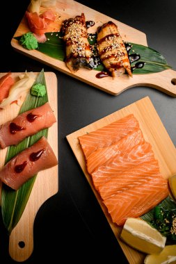 Suşi ve rulo siyah arka plandaki tahta tahtalara kurulur. Yeşil yaprak, yosun, wasabi, zencefil ve limon turşusu.