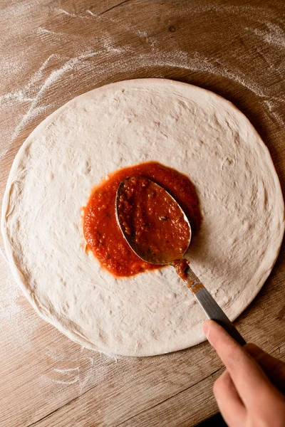 Şef hamurun üzerine titizlikle domates ezmesi serpiştirir. Mutfak başyapıtlarının tadını zenginleştirir..