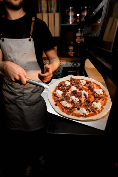 With a steady hand, the chef employs an oven shovel to transfer the pizza into the oven, marking the beginning of the baking process.