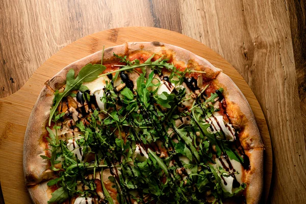 Yukarıdan bu yakından bakıldığında, pizza bir sanat eserine dönüşür. Taze roka eklenerek, lezzetli bir mutfak deneyimi için kırsal bir ahşap tahtada sunulur..