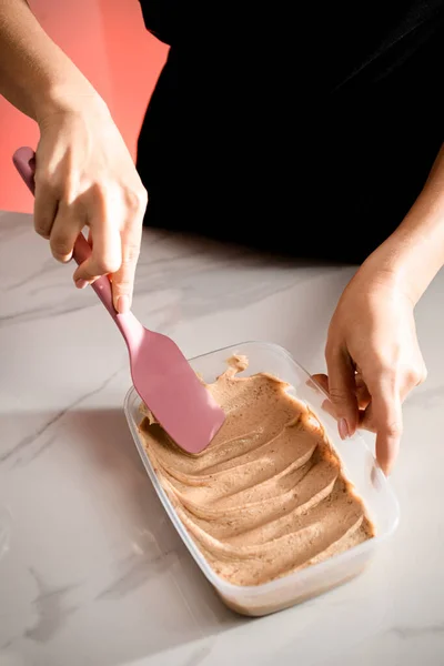 菓子の女性の手はプラスチック容器の底に均等に茶色のマカロン クリームを配ります — ストック写真