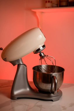 Büyük bir çırpıcı ve metal bir kase ile karıştırıcı beyaz bir mutfak masasında duruyor.