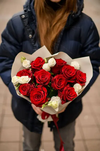 Tenderness bouquet of red and white flowers in the hands. Hidden face of a young girl who stands on a street