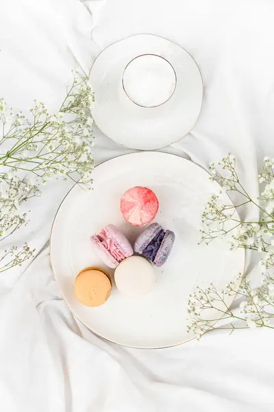 White flowers and exotic macaroons in a white plate on a white satin. Beautiful arrangement. Bouquet of the charming flowers