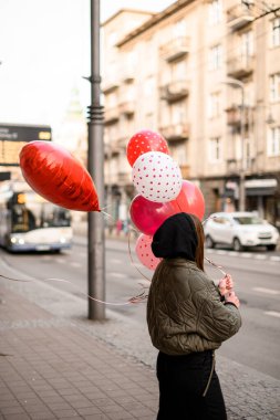 Gri ceketli, siyah kapüşonlu, elinde güzel bir buket kırmızı çiçekle genç bir kız.