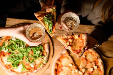 Bir bardak şarap ve pizza. Kızlar tatil için masada peynirli aromalı pizza yerler.