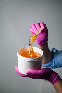 Beyaz plastik bir kabın içinde, ince ahşap bir spatulayla pembe eldivenli bal şekeri ya da balmumunu yapıştırmak için.