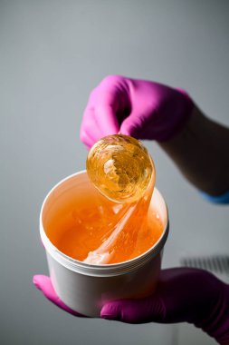 Şekerleme ustası pembe lastik eldivenlerle şeker ezmesi ve gri arka planda bir spatula.