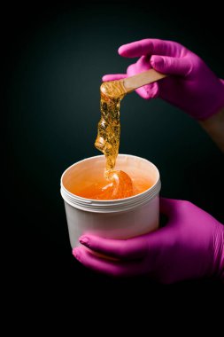 Depilation ustası elinde pembe lastik eldivenlerle ballı ya da şekerli siyah bir arka planda