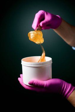 Plastik bir kabın içindeki yumuşak şekerleme macunu. Ellerinde pembe eldivenler ve koyu yeşil bir arka plan.