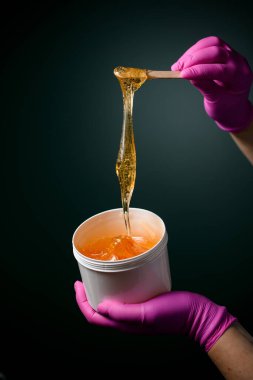 Beyaz plastik bir kabın içinde şeker veya bal içeren pembe lastik eldivenlerle sürme ustası.