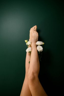 Koyu yeşil arka planda beyaz güllerle tüy dökme işleminden sonra düz açık tenli kadın bacakları.