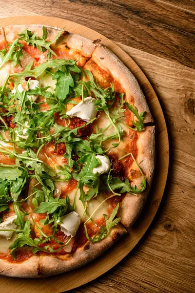Arugula ve bitkilerle sulu peynirli pizza, mozzarella ve krem peynir yuvarlak ahşap bir tezgahta.