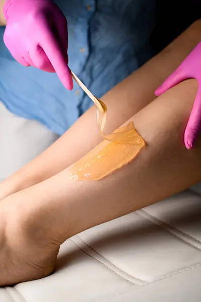 Sugaring depilation with sugar paste or wax honey. Master in white jeans and a blue shirt and pink rubber gloves