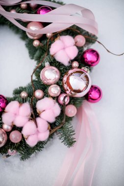 Yılbaşı çelengi kar arkaplanında. Yumuşak pembe bir çelenk ve gözlüklerle süslenmiş Noel ağacı oyuncakları.