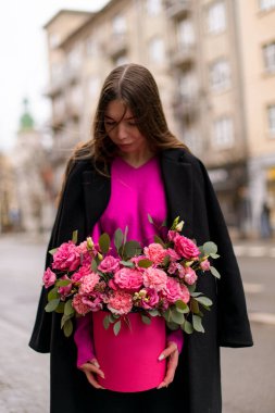 Genç ve güzel bir kadın hediye kutusunda başını eğmiş bir buket çiçek tutuyor.