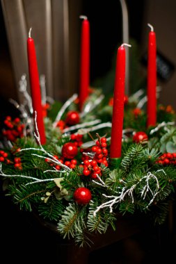 Kırmızı böğürtlenlerle süslenmiş Noel ağacı çelengi, bulanık arka planda dört kırmızı mumla süslenmiş beyaz dallar.