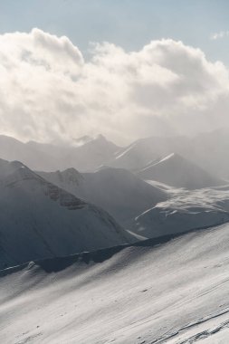 Güzel dağ manzarası, karla kaplı dağ sıraları sisle örtülmüş beyaz bulutlu mavi gökyüzünün arka planına karşı.