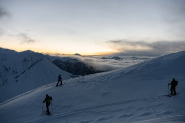 Üç kayakçı bir dağ yamacında mevzilenmiş. Böylece diğer dağlar yukarıdan görülebiliyor ve sis altında kalıyorlar.