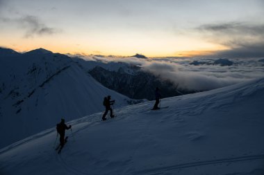 Üç kayakçı en yüksek dağın zirvesine tırmanır, böylece diğer zirveler yukarıdan görünür olur ve sis tarafından yutulur.