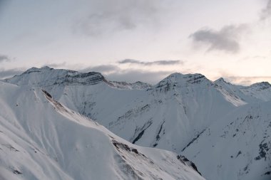 Tepeleri karla kaplı dağ yamaçlarının genel görünümü gün doğumuyla birlikte gökyüzünün arka planına karşı
