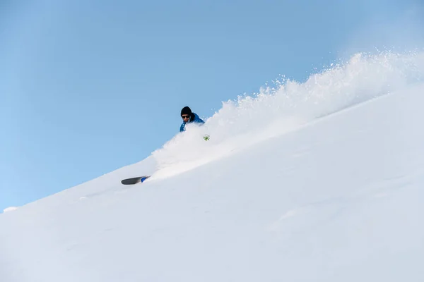 身穿蓝色夹克的男子滑雪者从雪地的斜坡上滑下去 几乎看不见他在粉末雪后面的影子 — 图库照片