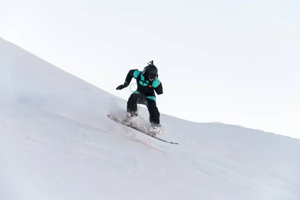 独臂男子滑雪板手在雪板上做了一个滑行的动作 使雪片飞向不同的方向 他自己也被悬挂在空中 — 图库照片