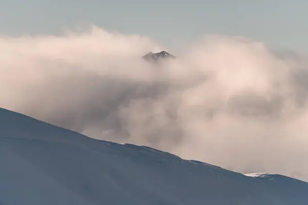 山間に広がる厚い霧のためにほとんど見えない山頂の背景の雪の斜面 — ストック写真