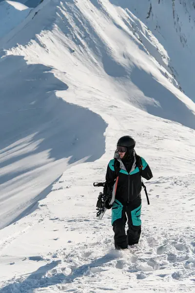 独臂男子滑雪板手提着雪板在山脊上的一座雪山上行走 — 图库照片
