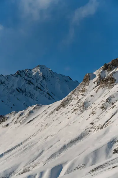 雪坡与蓝蓝的天空融合在一起 美丽的冬日清晨山景与棕色的山崖在雪地中窥视 — 图库照片