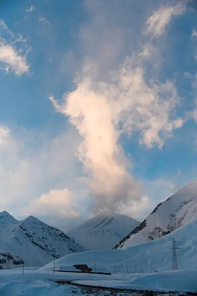 在蓝蓝的天空下 白云密布着 一辆覆盖着积雪的山地大轿车展开 一条路在前方蜿蜒而过 — 图库照片