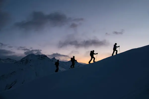 在高山最高处的四个滑雪者的轮廓 与雾中的山峰和红色的天空相对照 — 图库照片