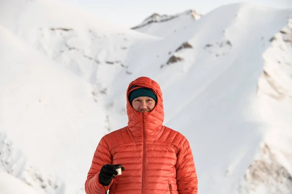 身穿红色夹克的男子滑雪者站在雪坡的后面 手里拿着一个金属杯子 手里拿着热茶 — 图库照片