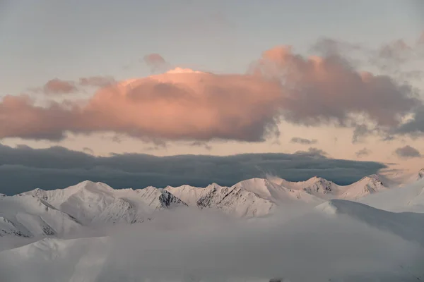在日落的天空背景上 山顶上覆盖着白雪和雾气 — 图库照片