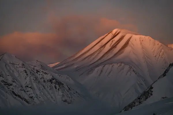山体的斜坡 在深红色的天空中 夕阳西下的光芒照亮了其中的一座山峰 — 图库照片
