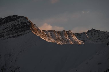 Koyu mavi gökyüzüne karşı kısmen karla kaplı sivri tepeli bir dağ yamacının yakın çekimi.