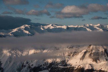 Güneşin doğuşuyla aydınlanan dağların tepeleri karların altında güzel bir dağ kitlesi. Dağların bir kısmı sisli çizgilerle kaplı.