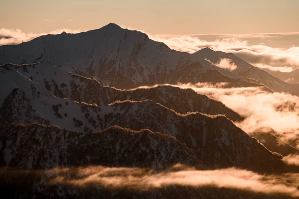 いくつかの山の斜面は互いに平行に配置され 部分的に雪と霧の雲で覆われ 日没時にクリムゾン色がついている — ストック写真