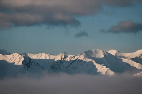 雪の下の美しい山の範囲 日の出の日の光に浴しているピークは 前景に霧の流れだけが見えます — ストック写真